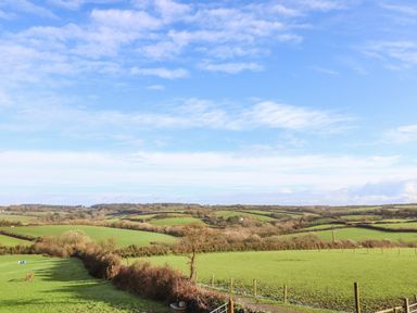 A landscape of green fields with trees and wind turbines under a partly cloudy sky at Valley View in Mullion