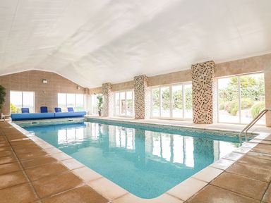 An indoor swimming pool with tiled floors and large windows at Valley View in Mullion