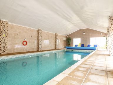 An indoor swimming pool with tiled walls and floor chairs and a pool cover at Valley View in Mullion