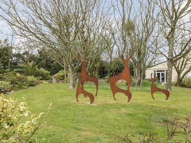 A garden with metal deer sculptures on grass surrounded by trees and plants at Valley View in Mullion