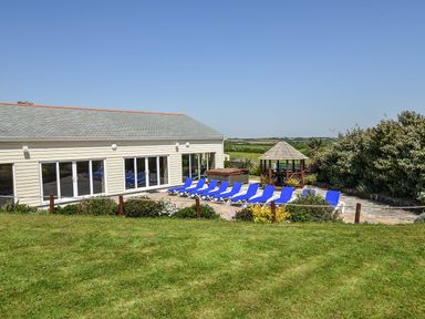 An outdoor patio area with blue lounge chairs a hot tub and a gazebo next to a building with large windows at Valley View in Mullion