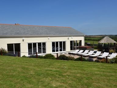 An outdoor area with a row of lounge chairs next to a building with large sliding glass doors and a gazebo in the background at Valley View in Mullion