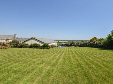 A large mowed grass lawn with bushes and buildings in the background at Valley View in Mullion