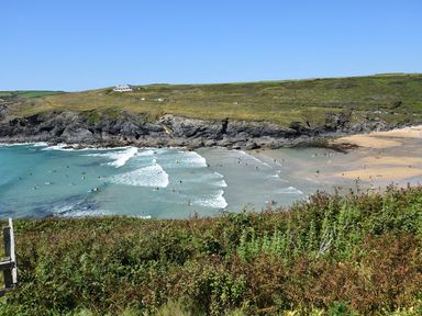A coastal beach with people swimming and surfing near rocky cliffs and grassy hills at Valley View in Mullion