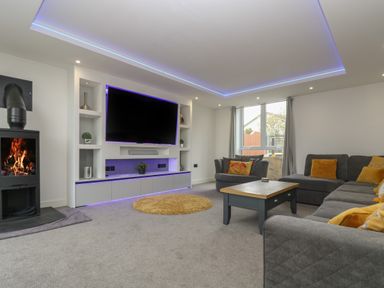 A living room with a large wall-mounted tv a fireplace and gray sofas at Valley View in Mullion