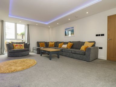 A living room with a large grey sofa yellow cushions coffee table and a round yellow rug at Valley View in Mullion