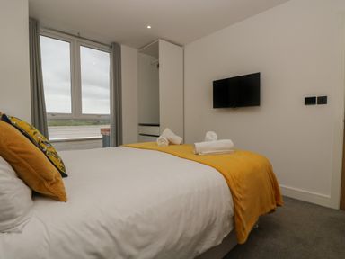 A bedroom with a bed with pillows and blankets a wardrobe a window and a wall-mounted television at Valley View in Mullion