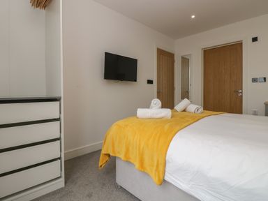 A bedroom with a bed covered with a yellow blanket and white towels with a wall mounted tv and wooden doors at Valley View in Mullion