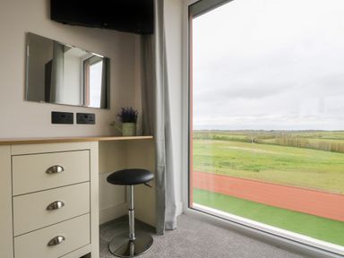 A corner desk with drawers a round stool a wall mirror and a window with a view of green fields at Valley View in Mullion
