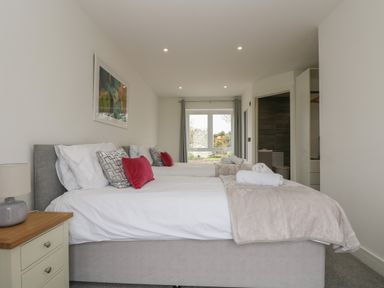 A bedroom with two beds gray headboards pillows and blankets a bedside table with a lamp and a window at Valley View in Mullion