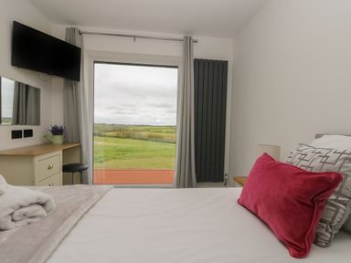 A bedroom with a bed a desk and a large window overlooking green fields at Valley View in Mullion