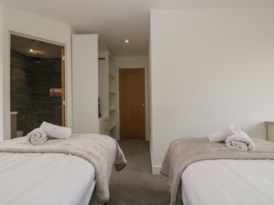 A bedroom with two beds with towels on them a wooden door and an open door leading to a bathroom at Valley View in Mullion