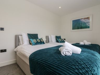 A bedroom with two single beds with white sheets teal blankets and pillows with rolled white towels on the beds at Valley View in Mullion