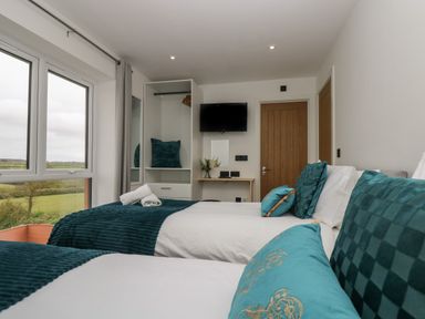 A bedroom with two beds with teal pillows and blankets next to a window and a wardrobe at Valley View in Mullion