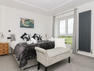 A bedroom with a bed, bedside tables, a cushioned bench, and a window showing green fields at Valley View in Mullion