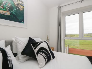 A bedroom with a bed with black and white pillows next to a window showing green fields at Valley View in Mullion