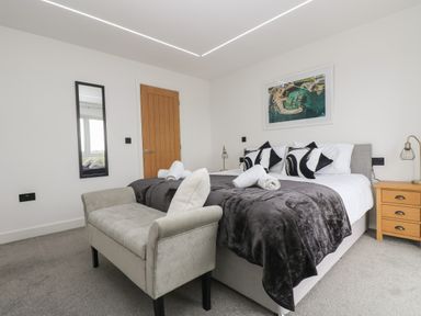 A bedroom with a double bed black and white pillows wooden bedside table and a bench at Valley View in Mullion