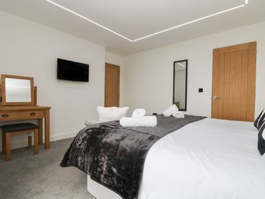 A bedroom with a bed with towels on it a wall mounted tv a wooden dressing table and a mirror at Valley View in Mullion