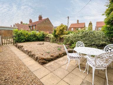 A garden patio with a white outdoor table and chairs next to a gravel area with plants at Tawny Cottage in Heacham