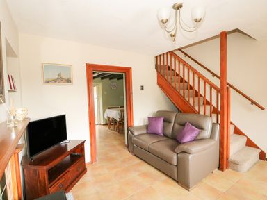 A living room with a sofa under stairs and television on a stand at Tawny Cottage in Heacham