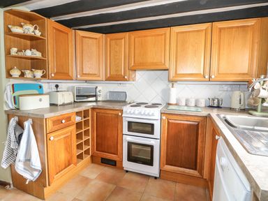 A kitchen with wooden cabinets an electric stove toaster microwave kettle and a sink at Tawny Cottage in Heacham