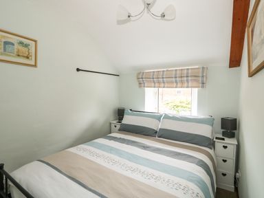 A bedroom with a double bed with striped bedding and two bedside tables with lamps at Tawny Cottage in Heacham