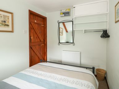 A bedroom with a bed near a wooden door a wall-mounted mirror shelves and hangers at Tawny Cottage in Heacham