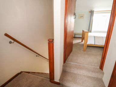 A carpeted staircase leading to a bedroom with a wooden bed frame and a window at Tawny Cottage in Heacham