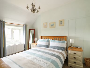 A bedroom with a double bed two bedside tables a mirror and three framed pictures on the wall at Tawny Cottage in Heacham