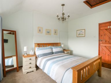 A bedroom with a wooden bed frame bedside tables and a standing mirror at Tawny Cottage in Heacham