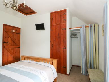 A bedroom with a wooden bed a wooden door built in wooden cupboard a small wall mounted TV and a striped curtain at Tawny Cottage in Heacham