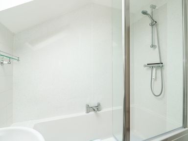 A bathroom with a bathtub shower combination and glass shower screen at Tawny Cottage in Heacham