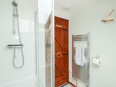 A bathroom with a shower area wooden door towel radiator and toilet paper holder at Tawny Cottage in Heacham