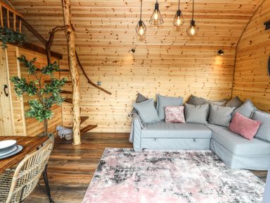 A living room with a grey sectional sofa with cushions wooden walls and a dining table with chairs at Offas Dyke Escape in St Asaph