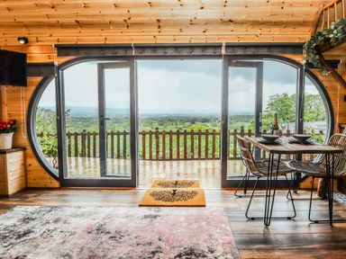 A wooden interior room with large glass doors opening to a balcony and a dining table with chairs at Offas Dyke Escape in St Asaph