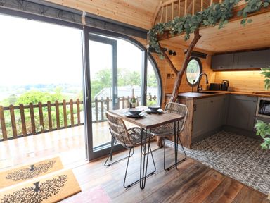 A dining area with a wooden table and two chairs next to large sliding glass doors and a kitchen with grey cabinets and patterned floor at Offas Dyke Escape in St Asaph