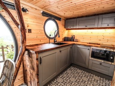 A kitchen with wooden walls gray cabinets patterned floor and a round window at Offas Dyke Escape in St Asaph