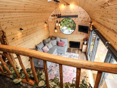 A wooden interior room with a gray sofa and pink cushions a round window hanging lights and a TV at Offas Dyke Escape in St Asaph
