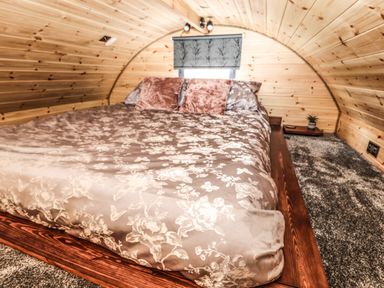 A bedroom with a bed covered with patterned bedding and pillows inside a wooden curved cabin at Offas Dyke Escape in St Asaph