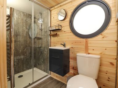 A bathroom with a shower, sink, toilet, round window, and wooden walls at Offas Dyke Escape in St Asaph