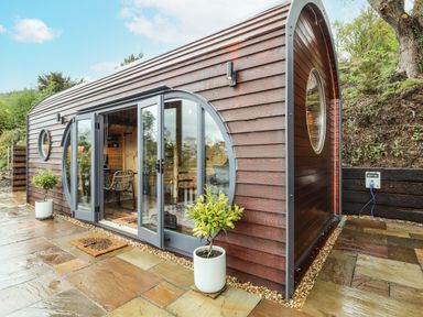 A curved wooden cabin with glass doors and circular windows on a stone patio with potted plants at Offas Dyke Escape in St Asaph
