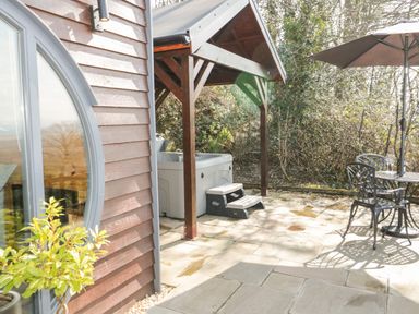 An outdoor patio area with a covered hot tub a metal table with chairs and an umbrella at Offas Dyke Escape in St Asaph