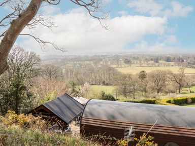 A rural landscape with fields and trees viewed from a hill above a wooden structure at Offas Dyke Escape in St Asaph