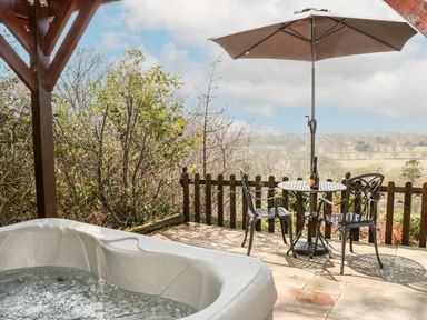 An outdoor patio with a hot tub two chairs a table with a bottle and a large umbrella at Offas Dyke Escape in St Asaph