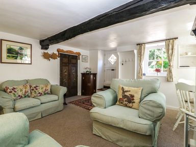 A living room with two armchairs and a sofa with decorative cushions a window with curtains and a door with hooks and a small cabinet at Small Piece in Porlock