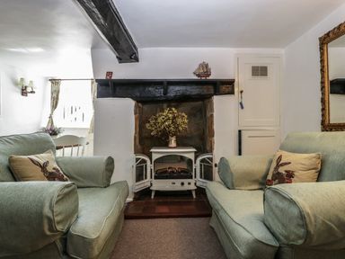 A living room with two cushioned armchairs facing a small electric stove under a black wooden mantel at Small Piece in Porlock