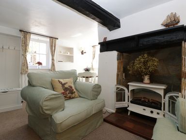 A living room with green armchairs a fireplace and windows with floral curtains at Small Piece in Porlock