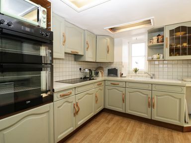 A kitchen with light green cabinets a double oven a microwave and a sink under a window at Small Piece in Porlock