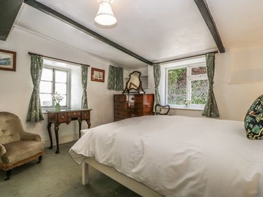 A bedroom with a bed a wooden dresser with a mirror a wooden table a chair and two windows with curtains at Small Piece in Porlock