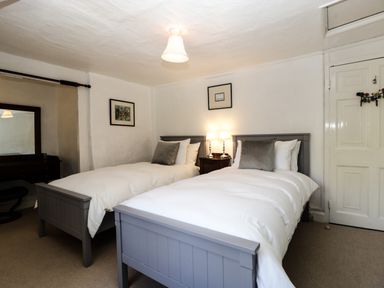 A bedroom with two single beds a bedside table with lamps a dresser with a mirror and two framed pictures on the wall at Small Piece in Porlock